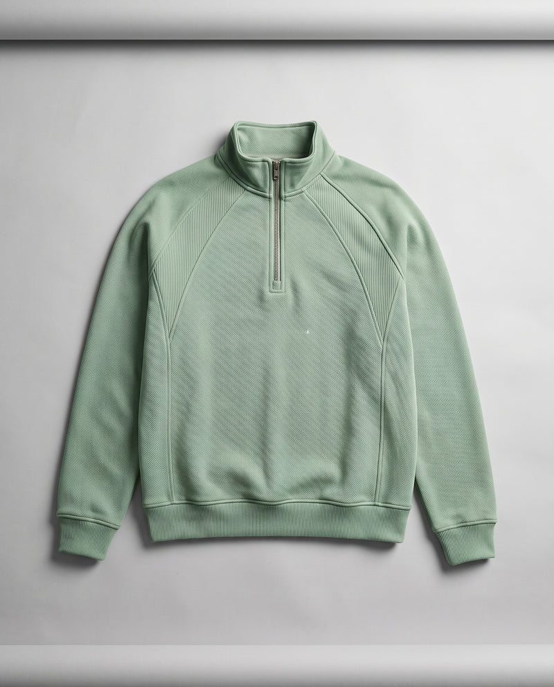 Sweat vert sauge pâle à demi-zip présenté à plat, entièrement déplié, avec col montant et fermeture éclair.