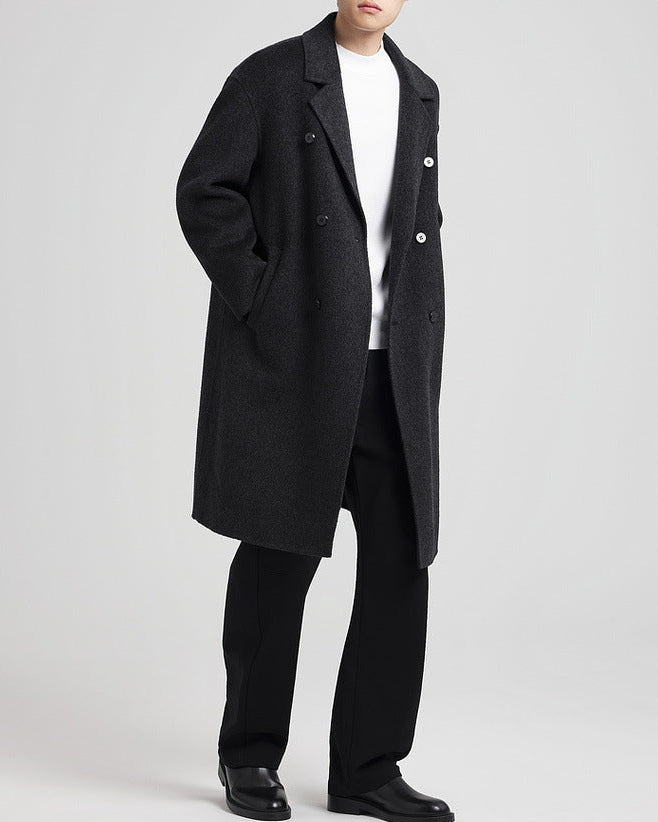 Manteau noir porté ouvert sur un t-shirt blanc avec un pantalon noir, en pied