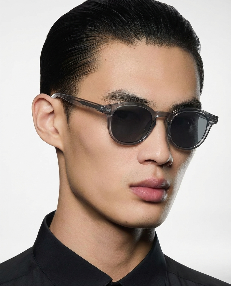 Homme portant des lunettes de soleil à monture ronde gris translucide à verres foncés, vue de trois quarts