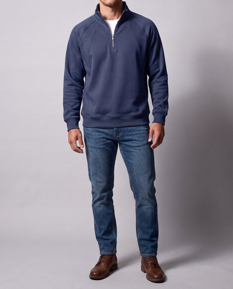 Vue de face en pied d'un homme portant un sweat bleu marine à demi-zip avec manches raglan et bas côtelé, avec un jean et des chaussures, sur fond studio neutre gris clair.