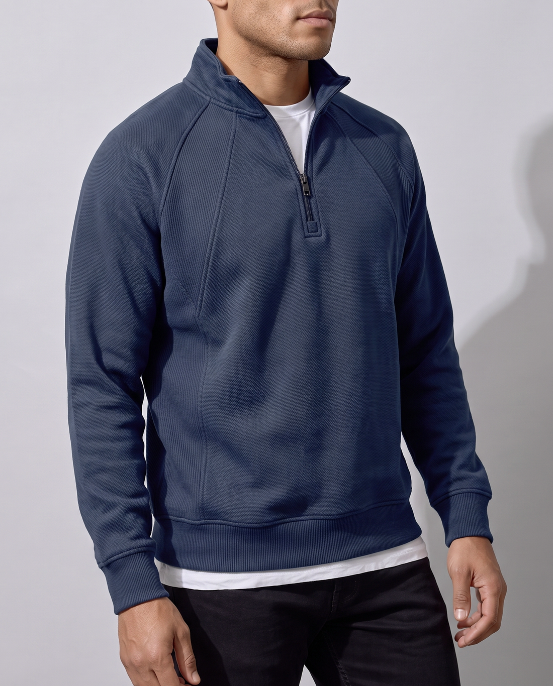 Vue de trois-quarts d'un sweat bleu marine à demi-zip montrant la couture raglane et le col montant, fond studio neutre.
