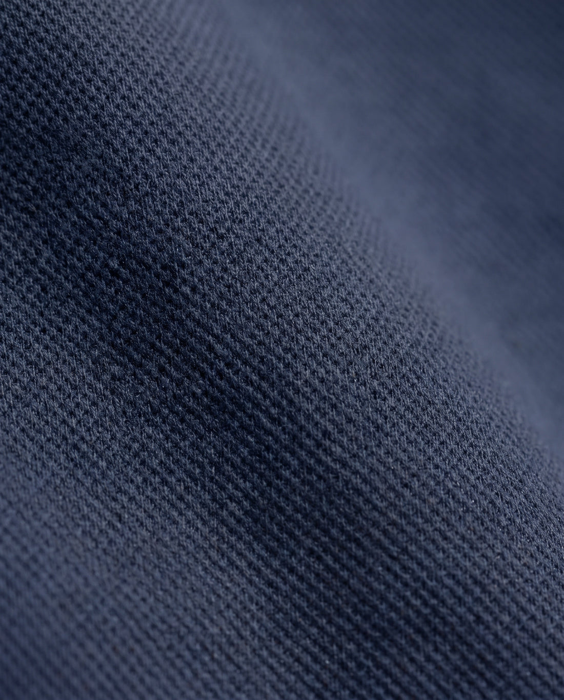 Gros plan sur la texture gaufrée du tissu du sweat bleu marine à demi-zip.