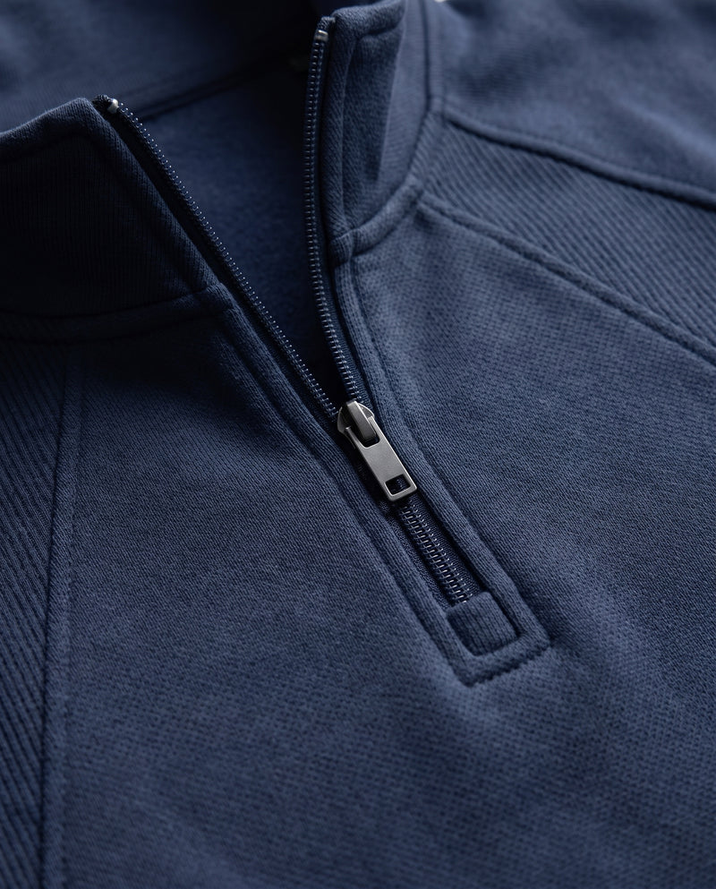 Gros plan sur la fermeture éclair métallique, le tirant rectangulaire et le col montant du sweat bleu marine à demi-zip.
