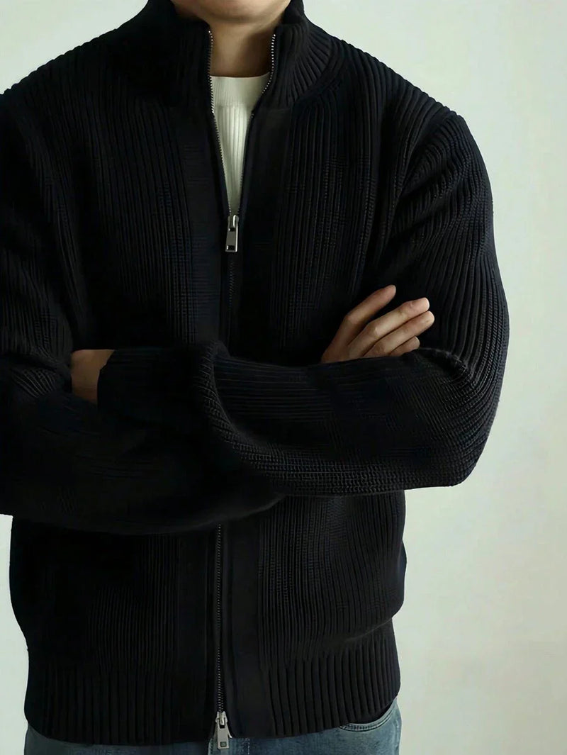 Black ribbed zip-through cardigan with a high collar, worn with arms folded