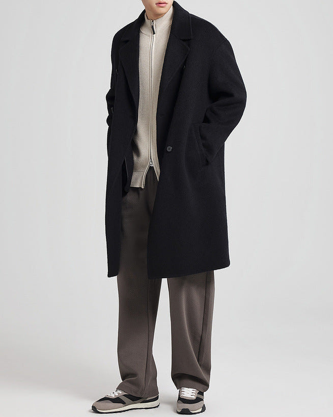 Manteau noir porté ouvert sur un haut crème avec un pantalon taupe, vue de face