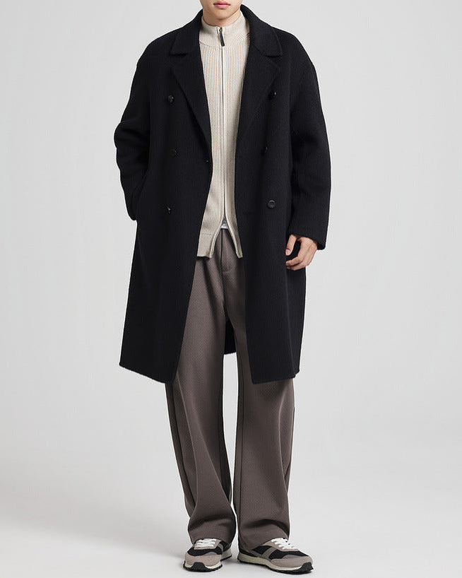 Black single-breasted overcoat worn open over a cream zip top with taupe trousers, full length