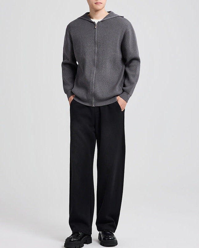 Cardigan en maille à capuche gris foncé porté avec un pantalon noir, les mains dans les poches