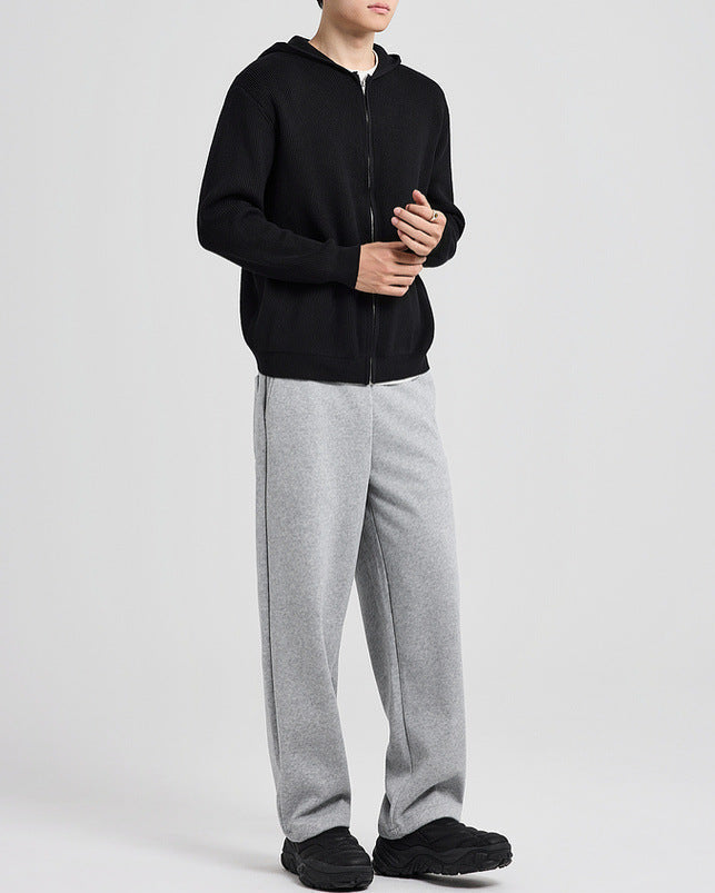 Cardigan en maille à capuche noir porté avec un pantalon gris, les mains jointes