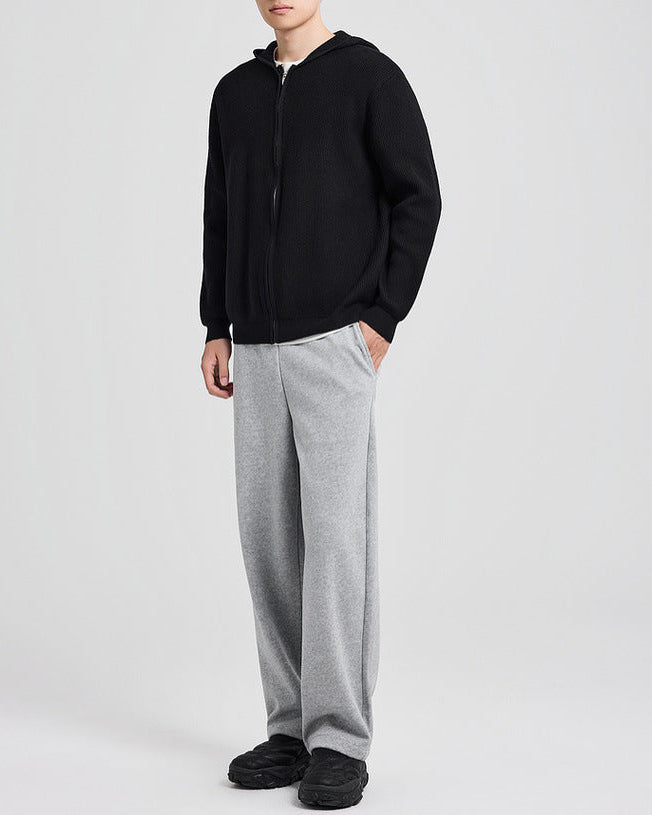 Cardigan en maille à capuche noir porté avec un pantalon gris, les mains le long du corps