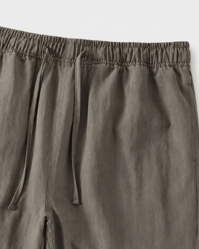 Gros plan sur la taille à cordon de serrage et la poche latérale du pantalon gris olive
