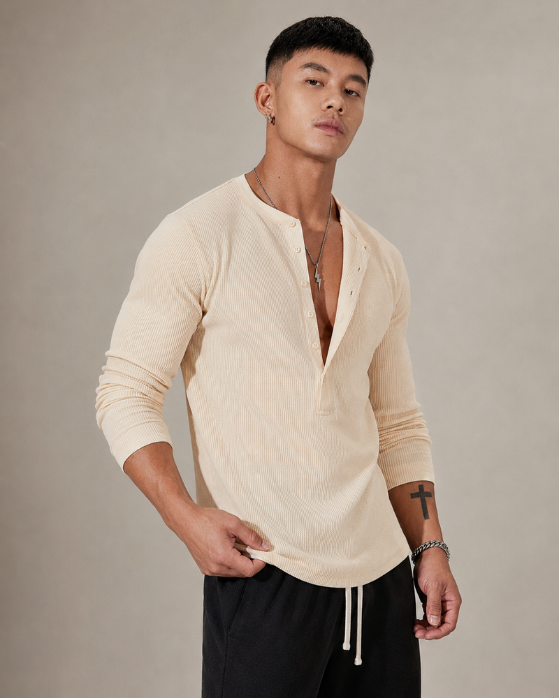 Pull Kade en maille côtelée écru porté par un mannequin, vue trois quarts, la main soulève le bas du pull pour montrer l’ourlet arrondi à finition plate étroite.