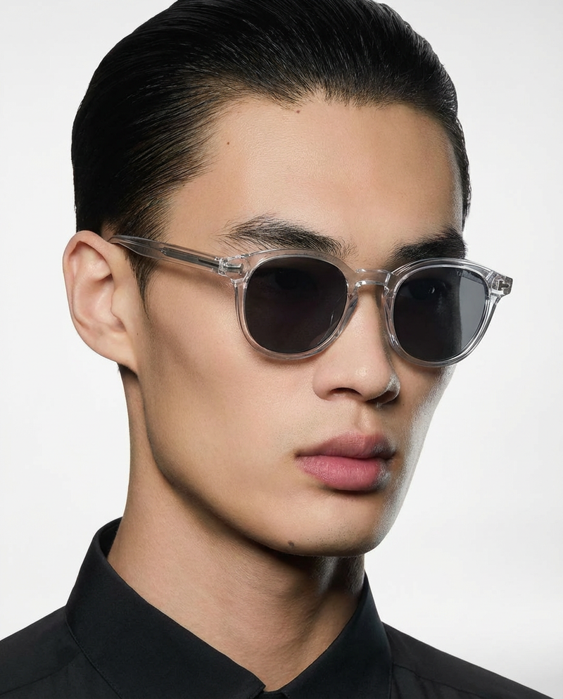 Homme portant des lunettes de soleil à monture ronde transparente à verres gris, vue de trois quarts