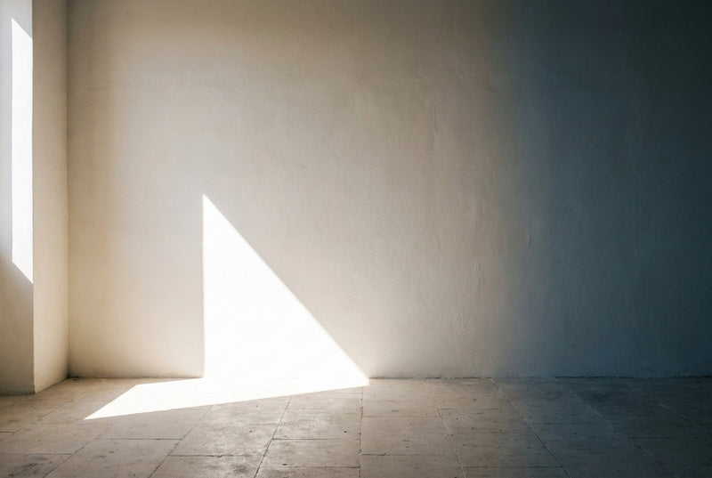 An empty whitewashed room with sunlight falling across a pale stone floor.