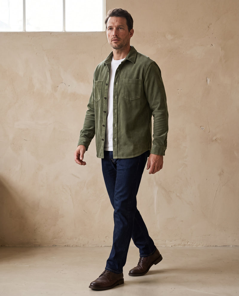 Man wearing an army green corduroy overshirt with dark indigo jeans and brown leather derby shoes, full length