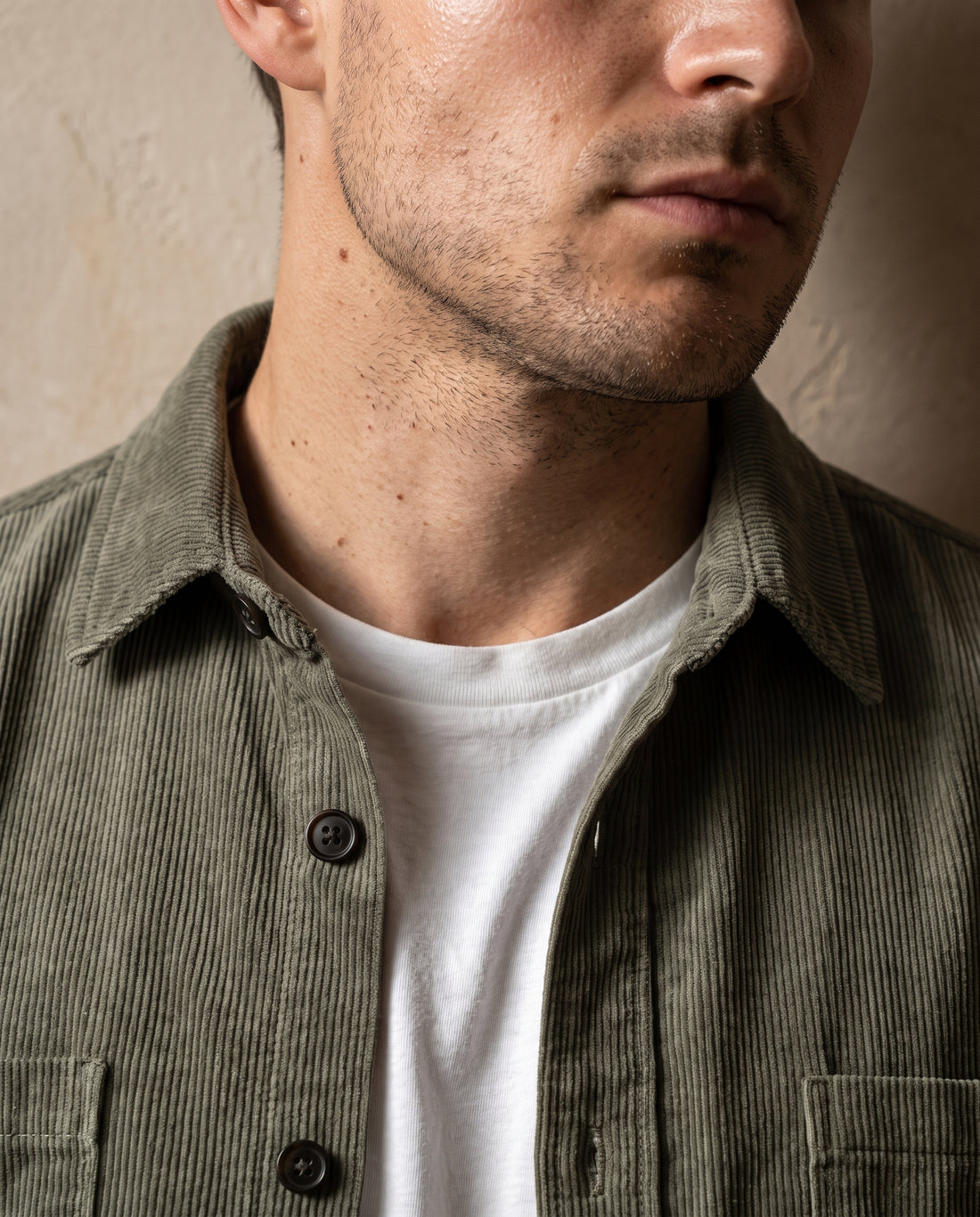 Close-up of the soft shirt collar and top button of an army green corduroy overshirt worn open over a white t-shirt