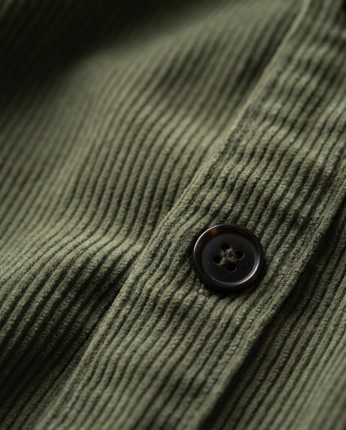 Macro of army green corduroy showing the narrow ribs and one dark brown-black four-hole button