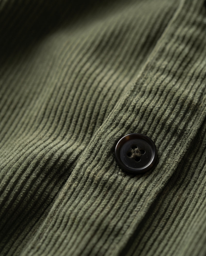 Macro of army green corduroy showing the narrow ribs and one dark brown-black four-hole button