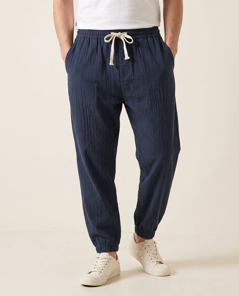 Homme portant un pantalon confort bleu marine, tissage froissé, cordon de serrage écru noué à la taille élastique, vue de face sur fond studio blanc cassé.