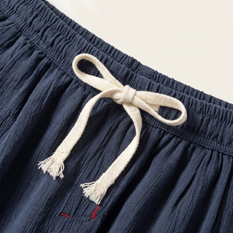 Détail de la taille élastique du pantalon bleu marine, cordon écru noué en nœud aux extrémités effilochées, petit détail de surpiqûre rouge.