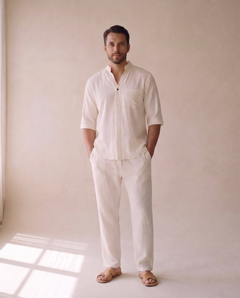 Homme portant une chemise ample à manches courtes écrue et le pantalon assorti à cordon de serrage, avec des sandales en cuir fauve, en pied