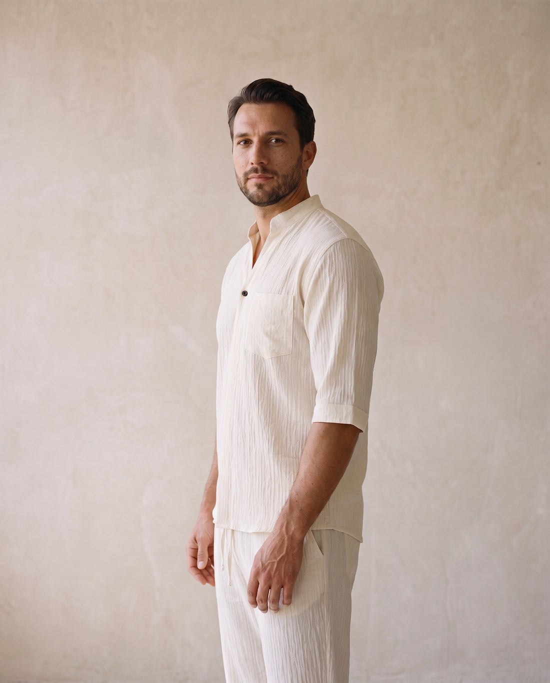 Man in an off-white two-piece shirt and trouser set, three-quarter view