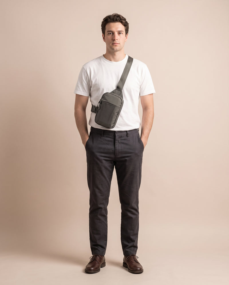 Homme portant la sacoche bandoulière gris olive avec un t-shirt blanc, un pantalon anthracite et des derbies en cuir marron, en pied