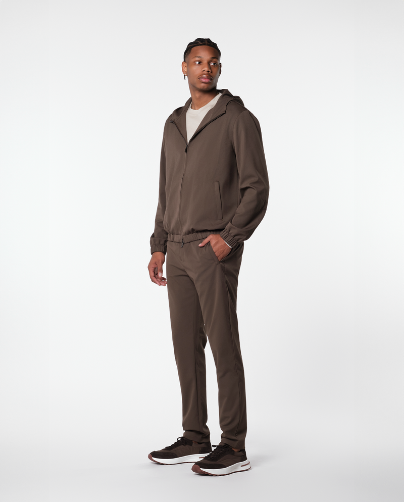 Homme portant une veste technique marron et le pantalon assorti, vue de profil en pied
