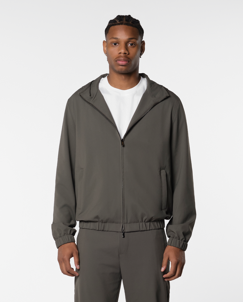Homme portant une veste coupe-vent à capuche vert olive ouverte sur un t-shirt blanc, vue de face