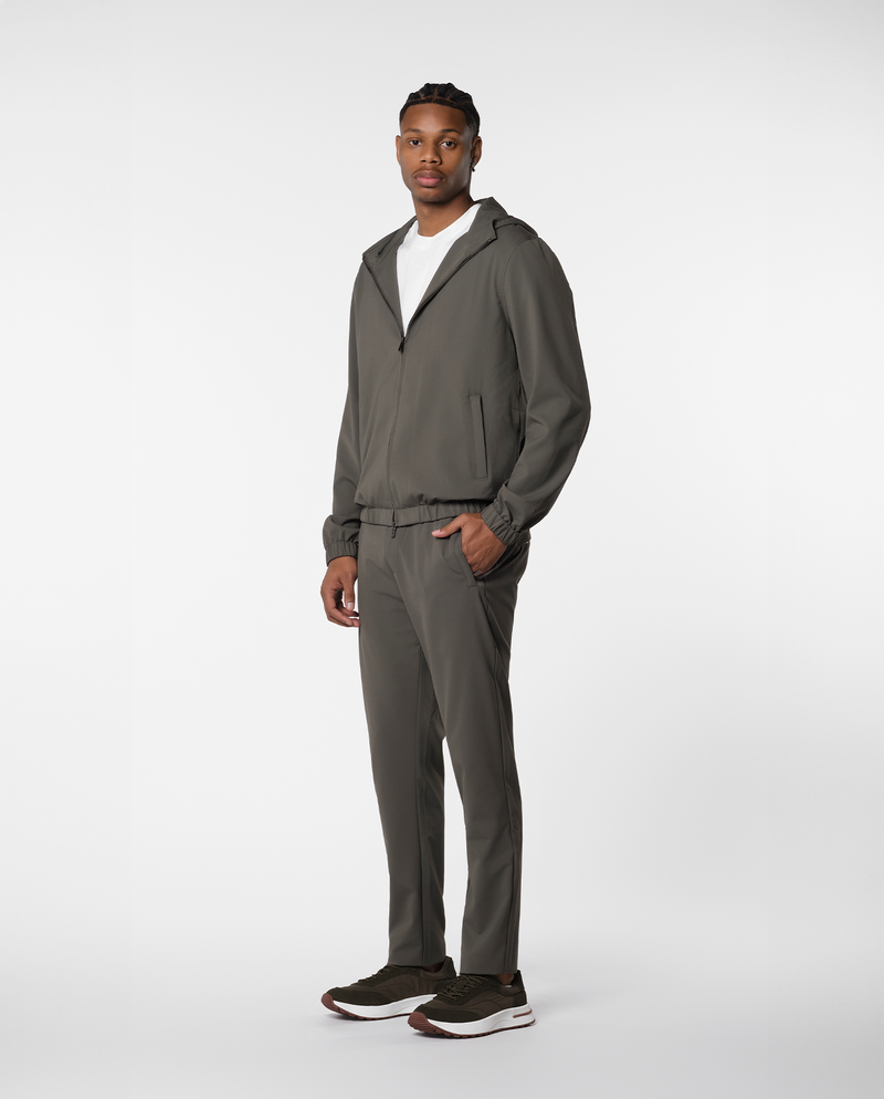 Homme portant une veste coupe-vent à capuche vert olive et le pantalon assorti, vue de profil en pied
