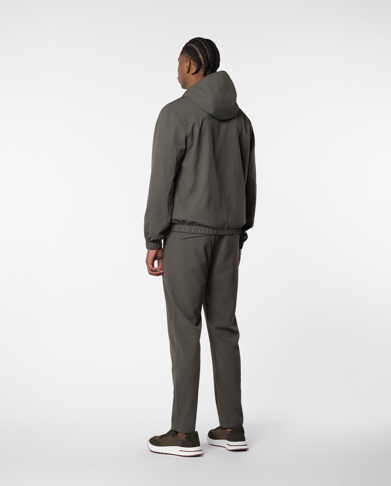 Homme portant une veste coupe-vent à capuche vert olive et un pantalon, vue de dos en pied