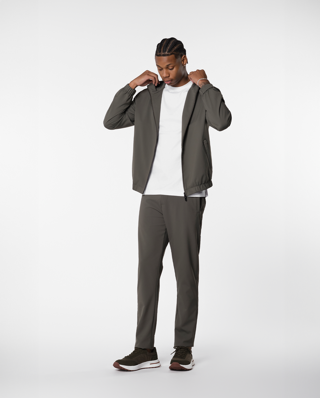 Man adjusting the hood of an olive-green shell jacket, full length front view