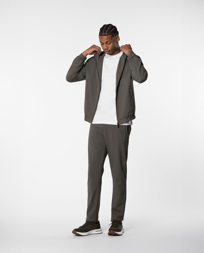 Homme ajustant la capuche d'une veste coupe-vent vert olive, vue de face en pied
