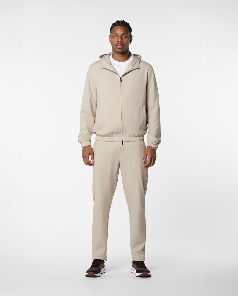 Homme portant une veste coupe-vent à capuche beige ouverte sur un t-shirt blanc, vue de face