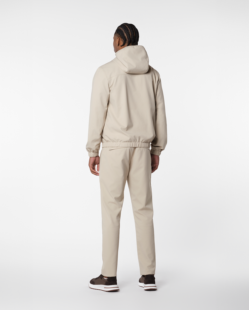Homme portant une veste coupe-vent à capuche beige et le pantalon assorti, vue de dos en pied