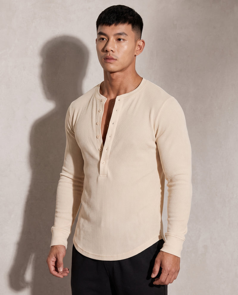 Pull Kade en maille côtelée écru porté par un mannequin, plan buste : demi-patte de boutonnage ouverte à six boutons tonals, encolure ronde côtelée sans col.