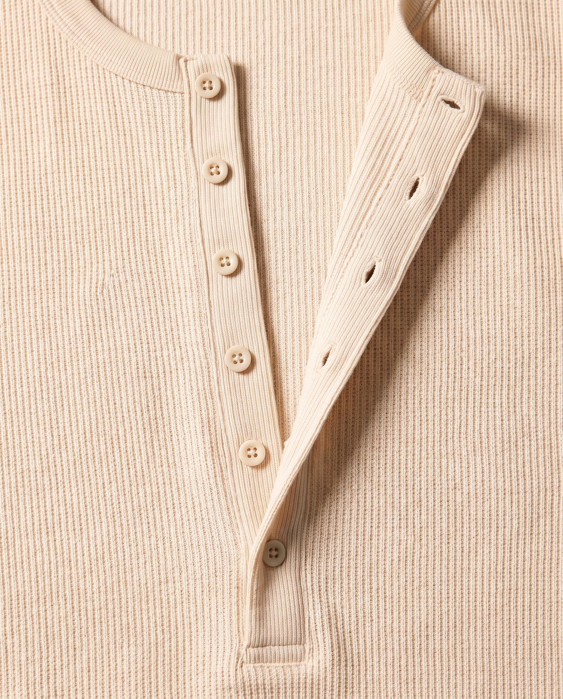 Gros plan sur la demi-patte de boutonnage du pull Kade écru : six boutons tonals plats et six boutonnières, bouton du bas fermé.