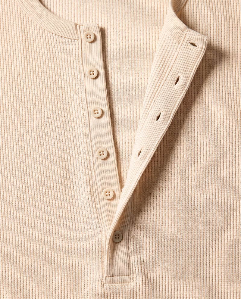Gros plan sur la demi-patte de boutonnage du pull Kade écru : six boutons tonals plats et six boutonnières, bouton du bas fermé.