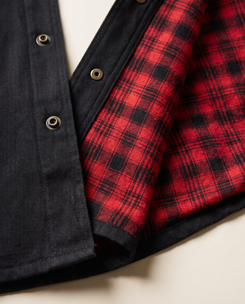 Gros plan sur le devant ouvert de la surchemise noire, révélant la doublure en flanelle à carreaux buffalo rouge et noir contre le tissu extérieur