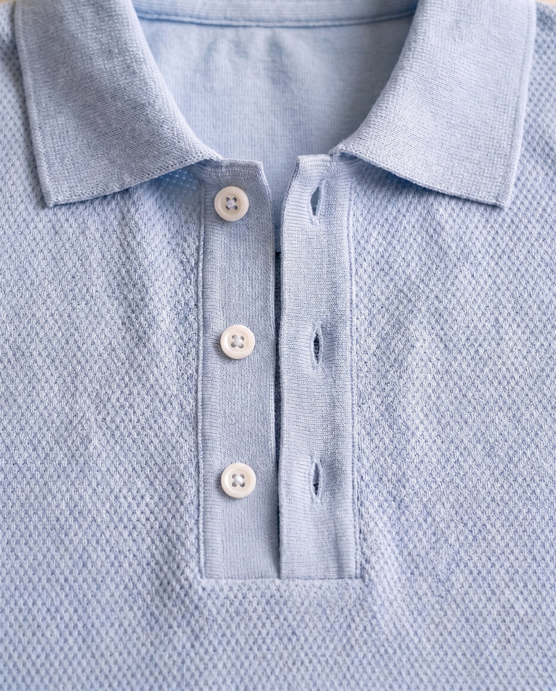 Gros plan sur le col en maille et la patte de boutonnage à trois boutons du polo bleu clair