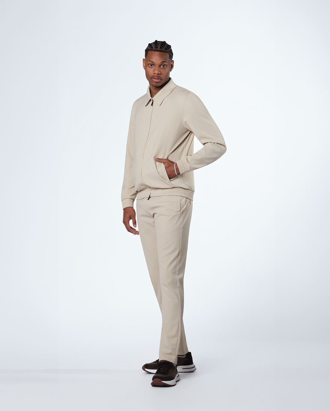 Man wearing beige trousers with a matching zip jacket, full length side view