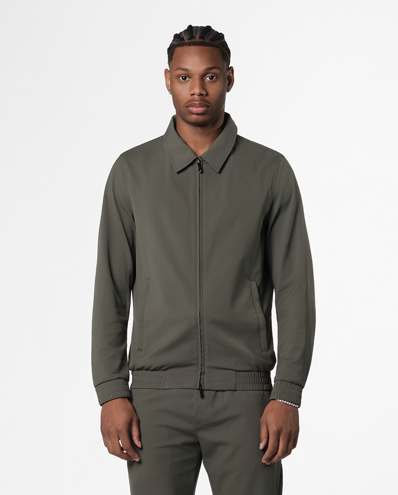 Man wearing an olive-green zip jacket with a flat collar and matching trousers, front view
