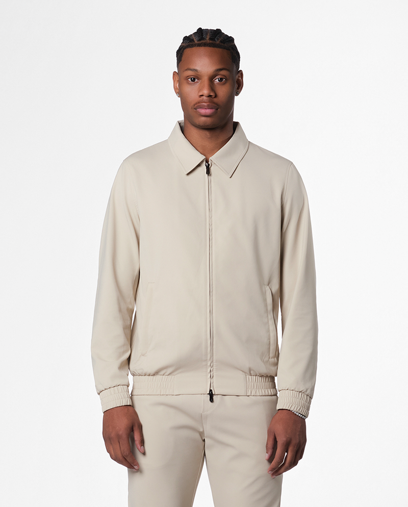 Man wearing a beige zip jacket with a flat collar and matching trousers, front view
