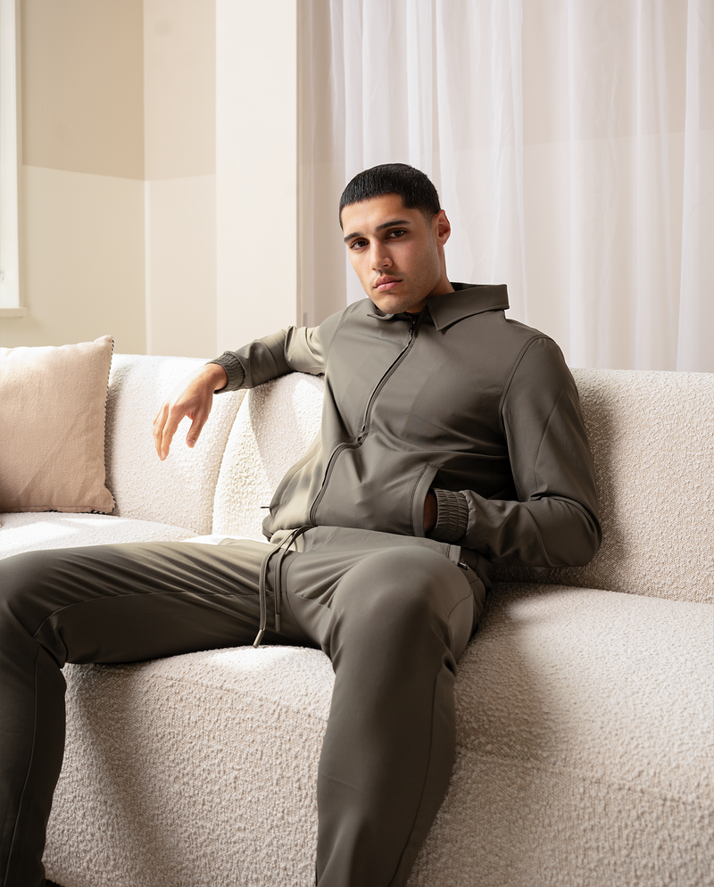 Homme en pantalon vert olive et haut à capuche assorti, assis sur un canapé crème